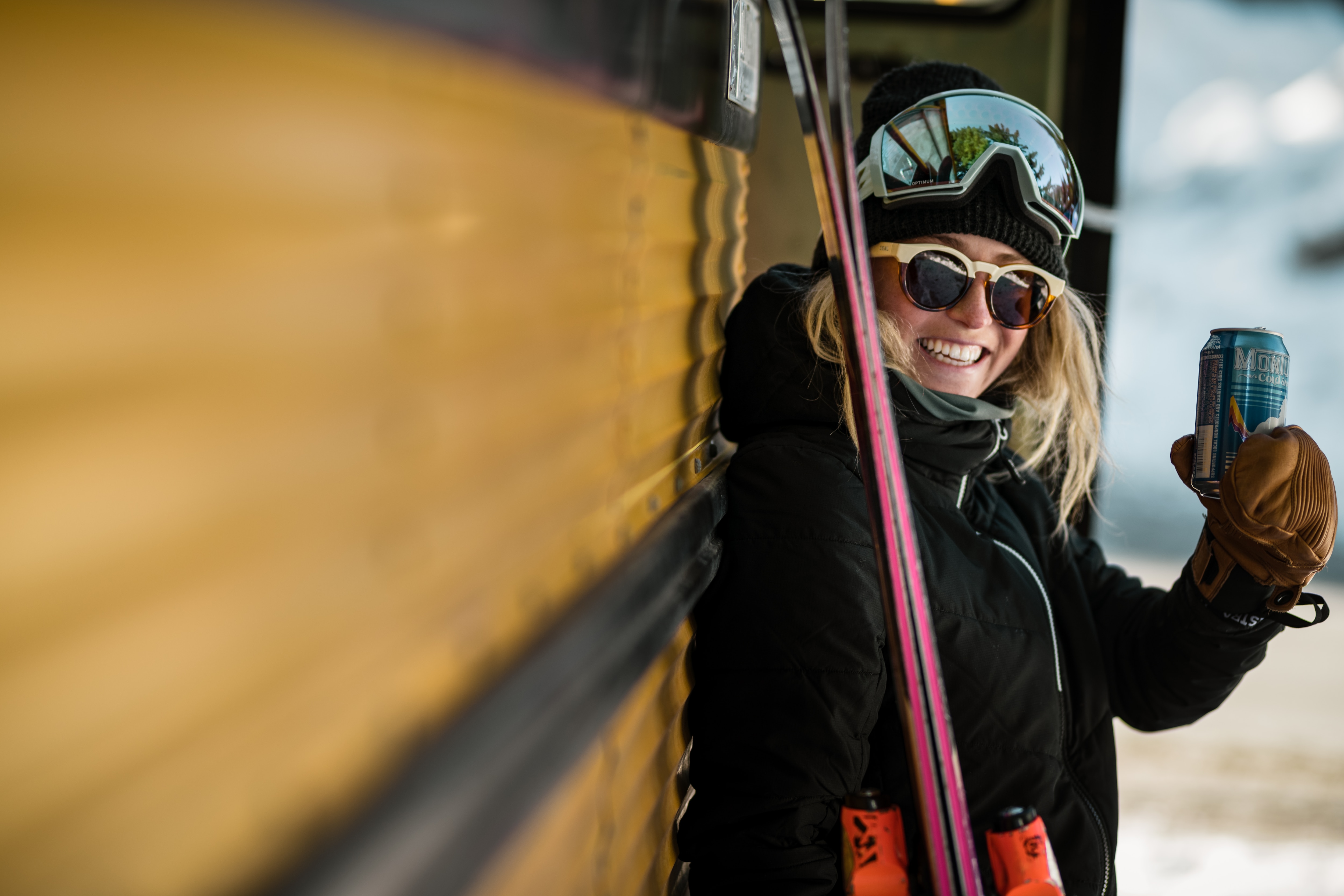 smiling skier leaning against a bus and holding up her drink