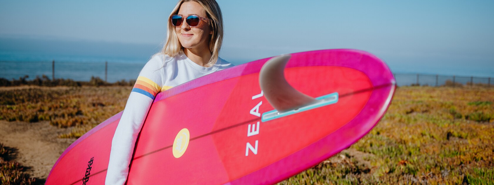 a woman with a bright pink surfboard wearing Zeal sunglasses