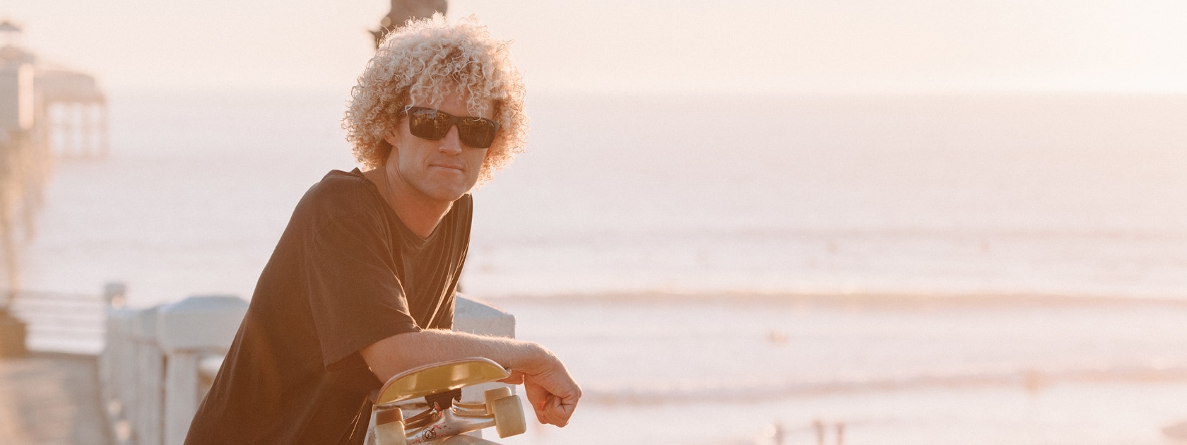 a man with a skateboard and wearing sunglasses near a beach