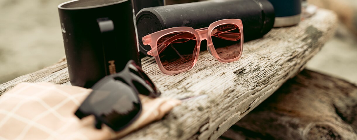 two Zeal sunglasses sit on drift wood on the beach
