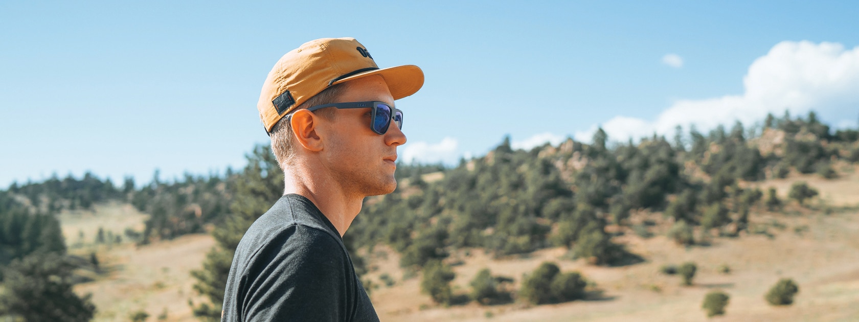 a man wearing sunglasses and hat standing in the mountains