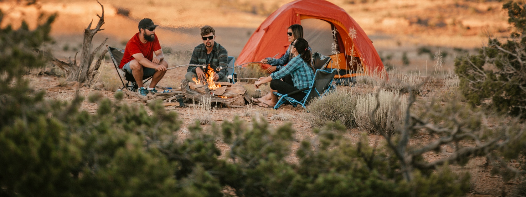 four people sit around a campfire making s'mores in the desert