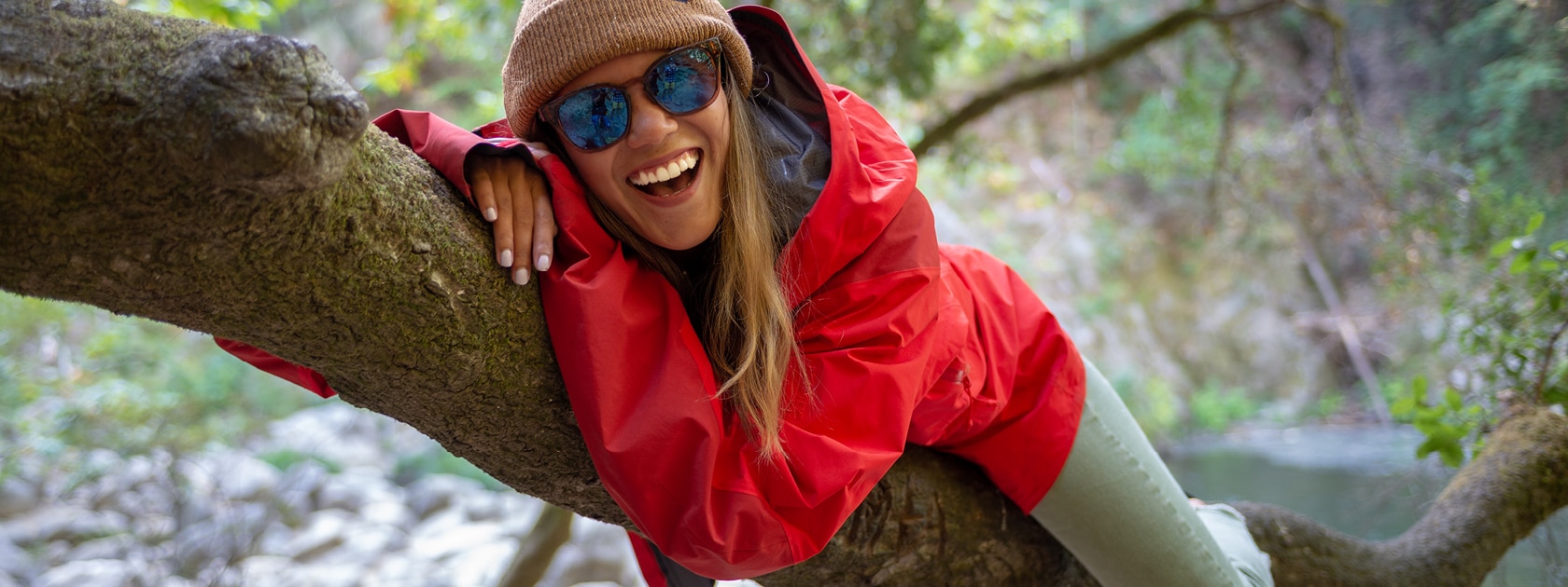 woman in a red jacket and sunglasses lies on a tree branch