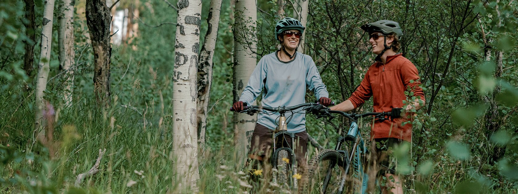 two people resting on their mountain bike wearing polarized sunglasses on a lush forested trail