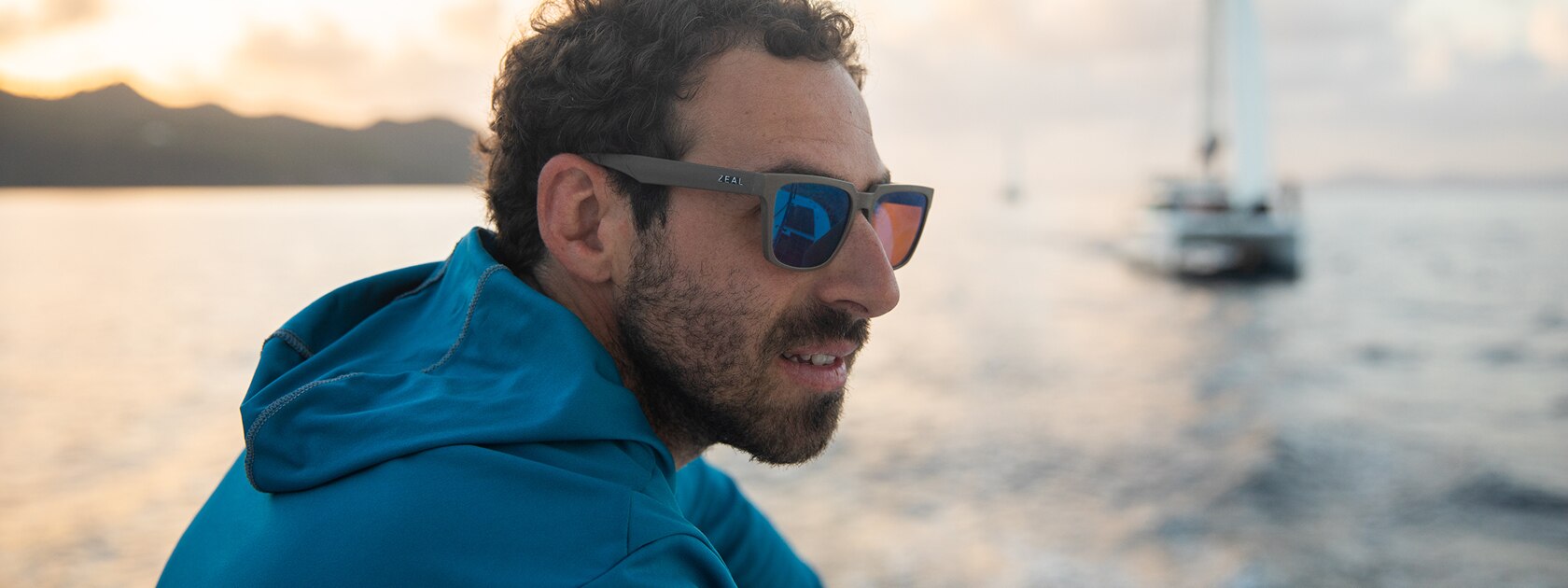 man wearing zeal northwind polarized sunglasses with an ocean and sailboat behind