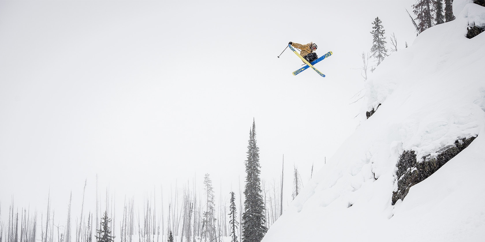 person flying through the air off a snow covered cliff wearing skiis
