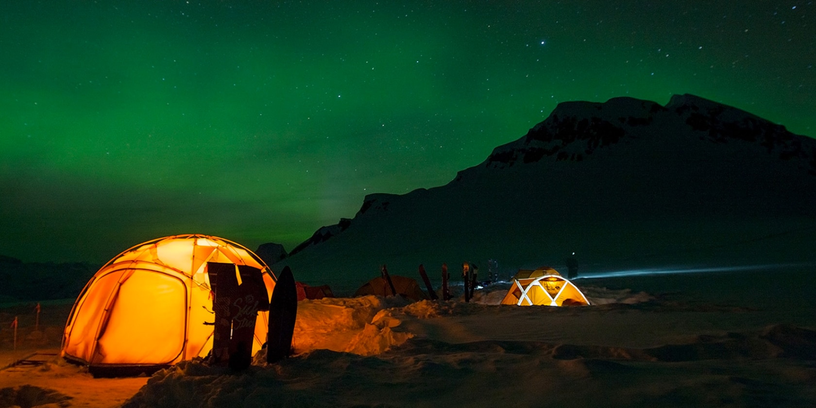 two tents glow from the inside as a green glow illuminates the sky above them
