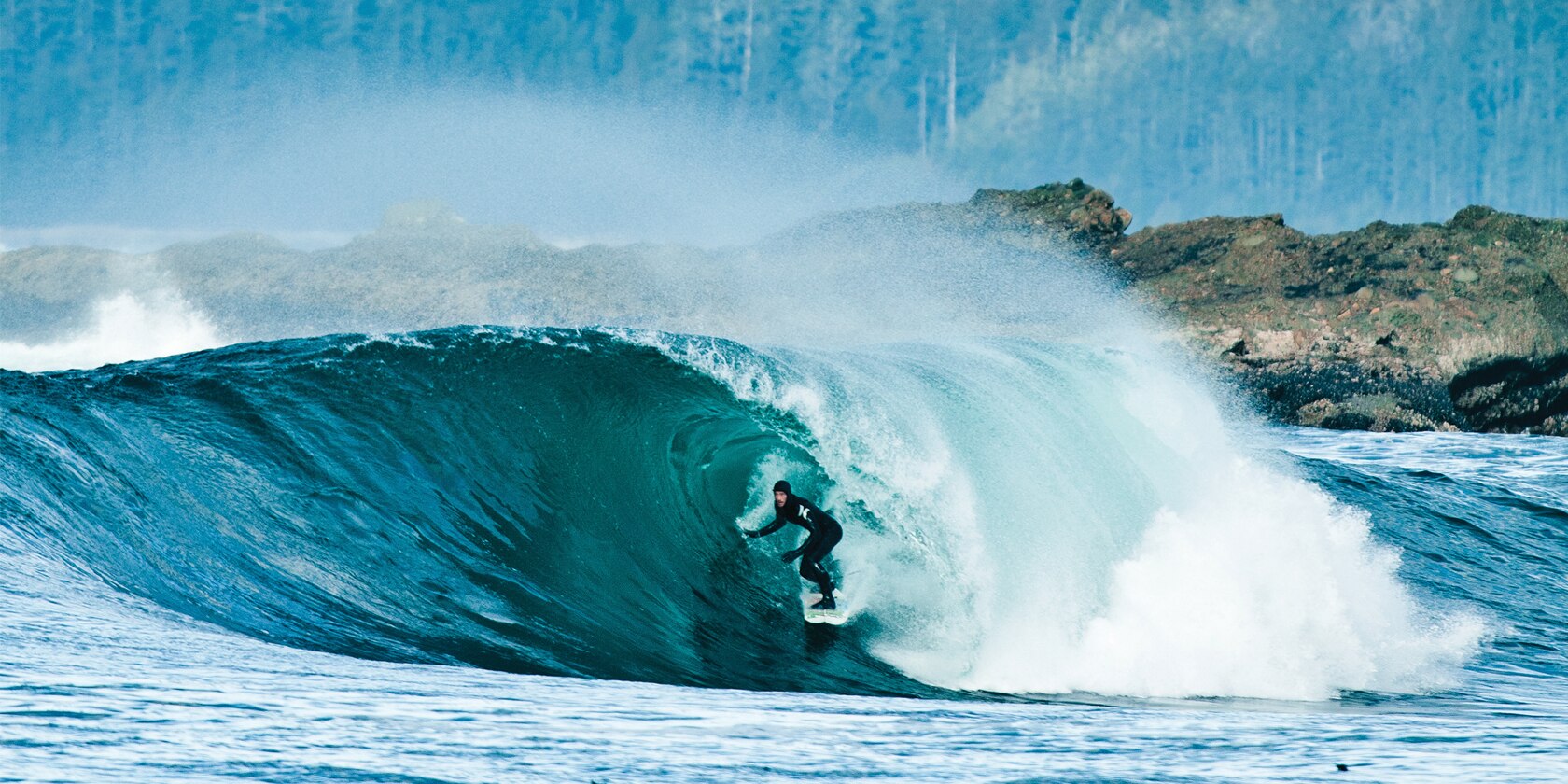 man wearing black wet suit surfing a large wave