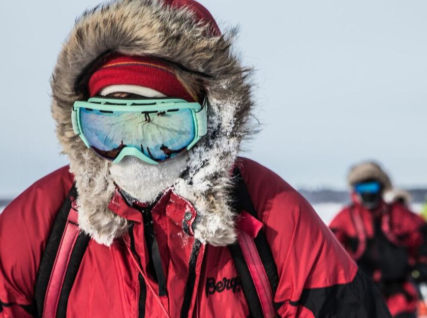 person with red and black coat with fur hood and blue lens ski goggles battles the cold