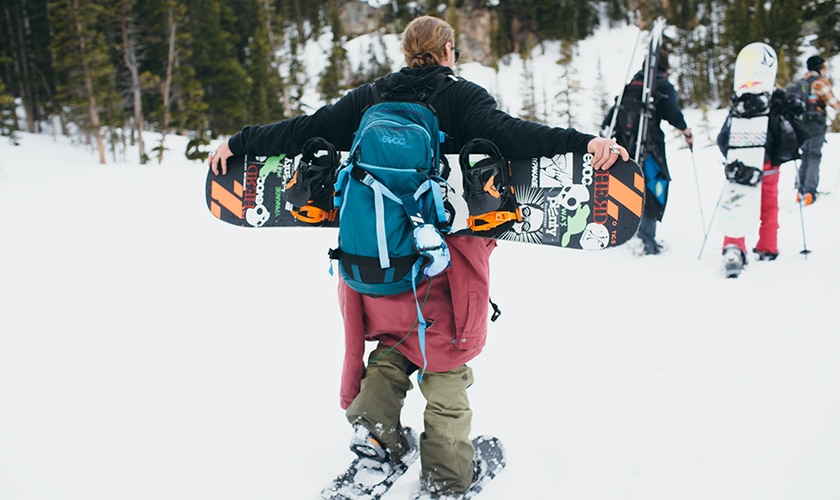 man carrying snowboard and backpack walking in the snow