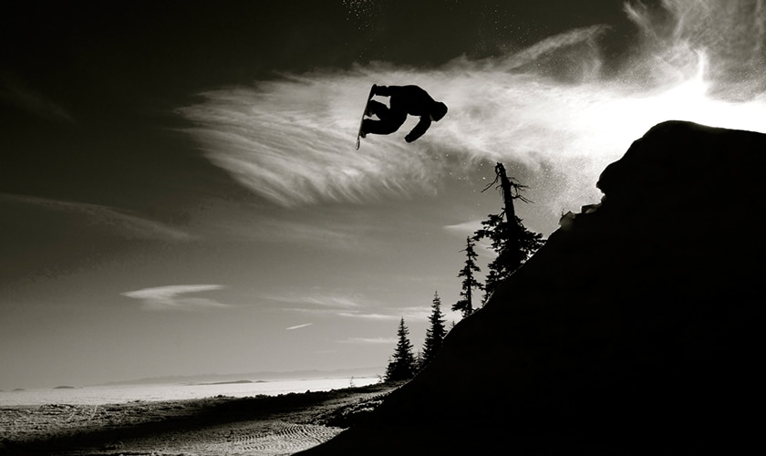 person doing flips in the air on a snowboard in black and white