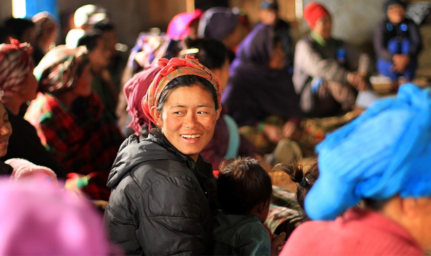 sitting woman with child in her lap in colorful head scarf smiling to the left