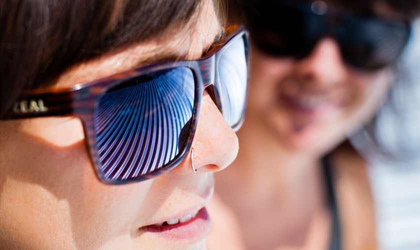 closeup view of two girls wearing sunglasses with window blinds reflecting in lenses