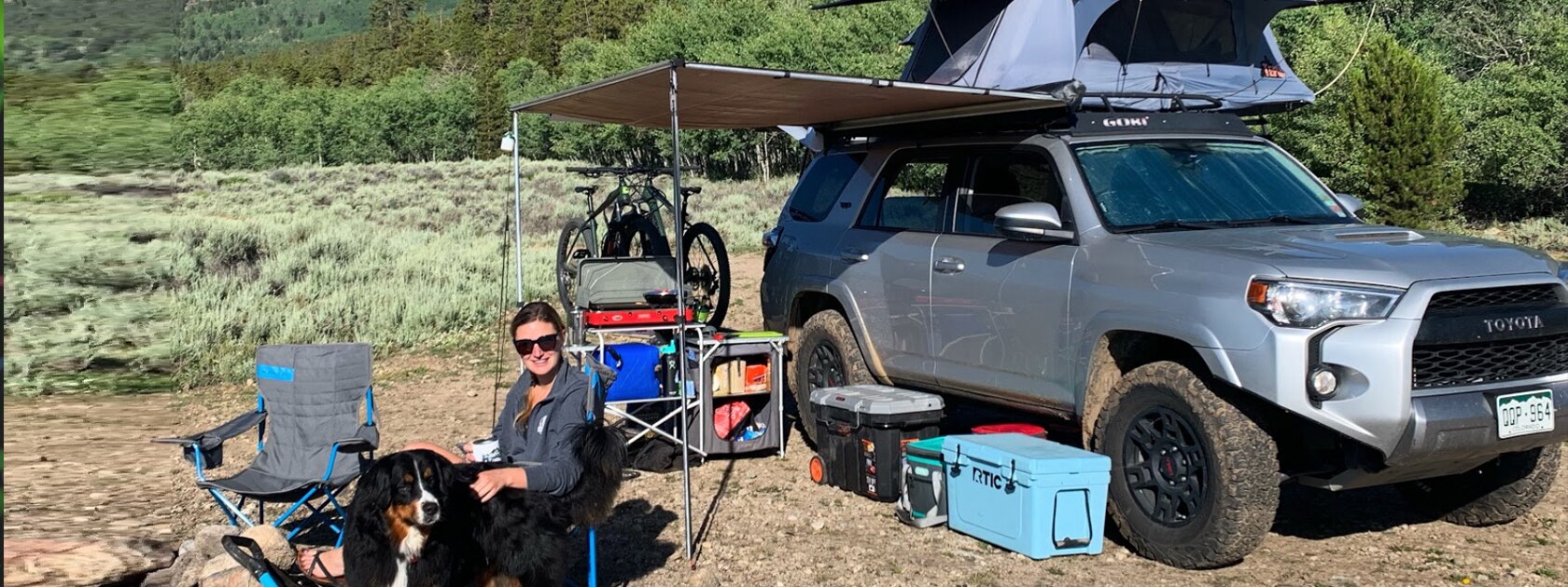 a woman and dog sit next to a 4Runner with a car camping setup
