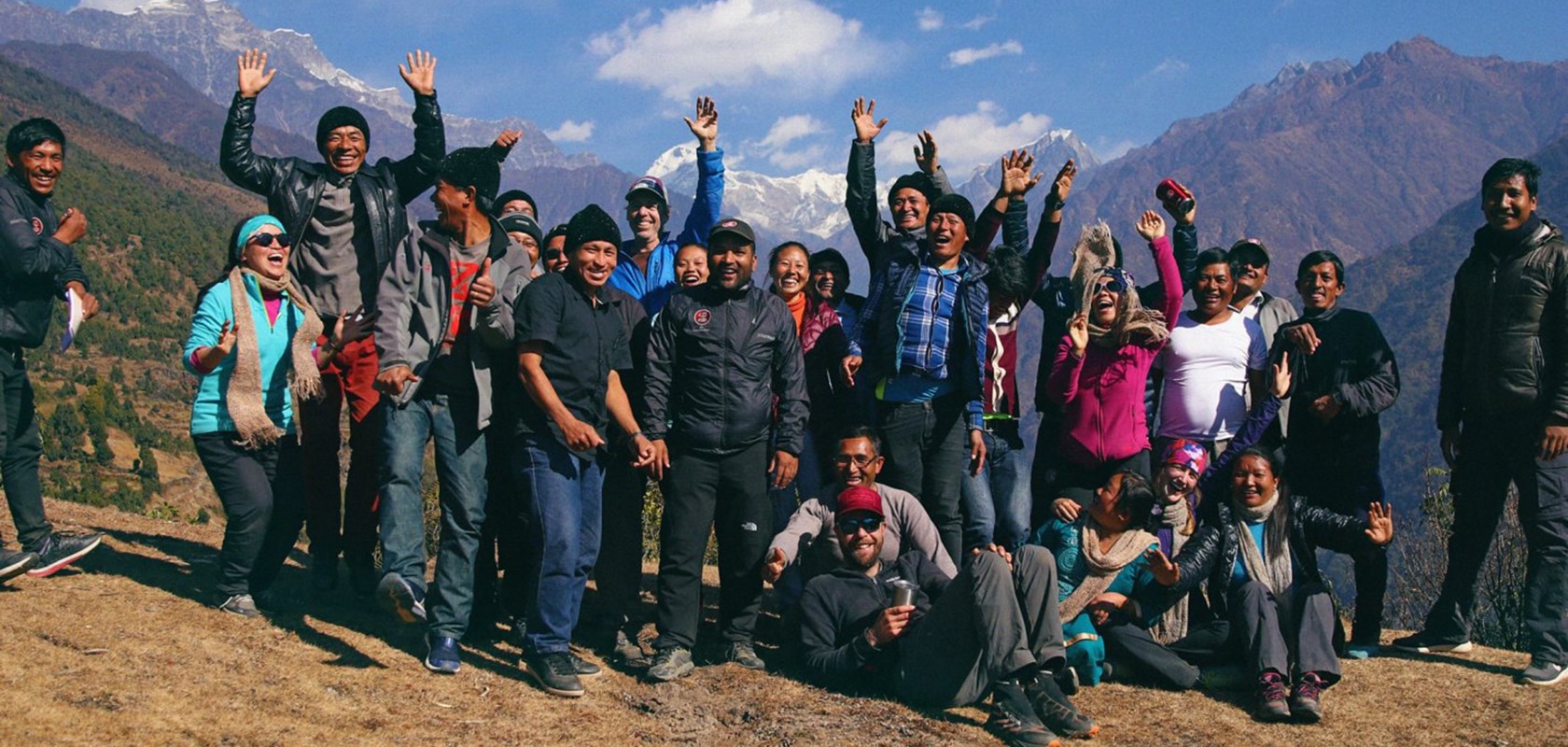 group of people smiling and cheering on a mountain path