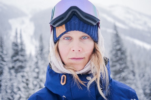 portrait of blue eyed woman with mirrored lens goggles on head standing in snowy mountains