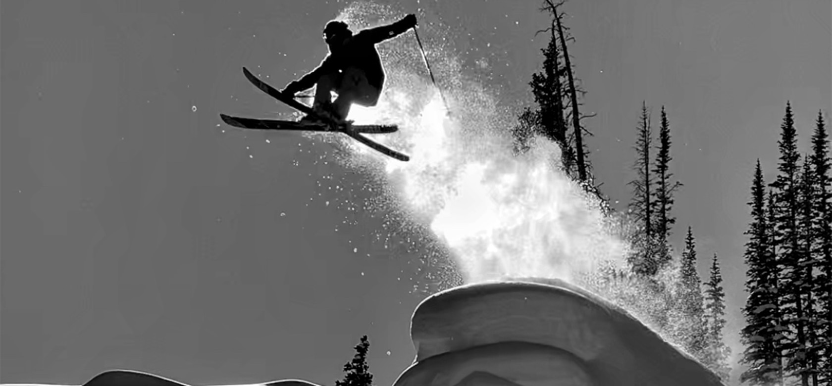 Black and white photo of Colter going off of a jump on skis 