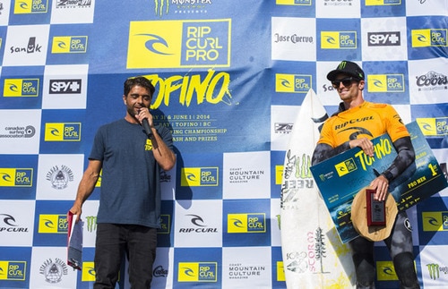 A man with a microphone presenting a surfing prize to another man on stage