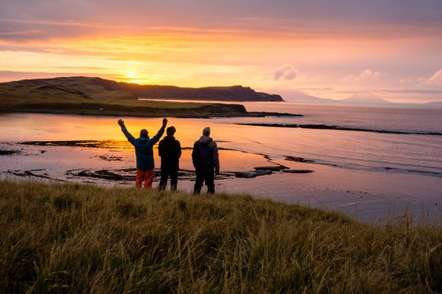 Three men standing on a beach watching a sunset