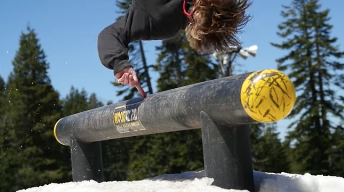 Snowboarder touching a course pipe while flipping over it