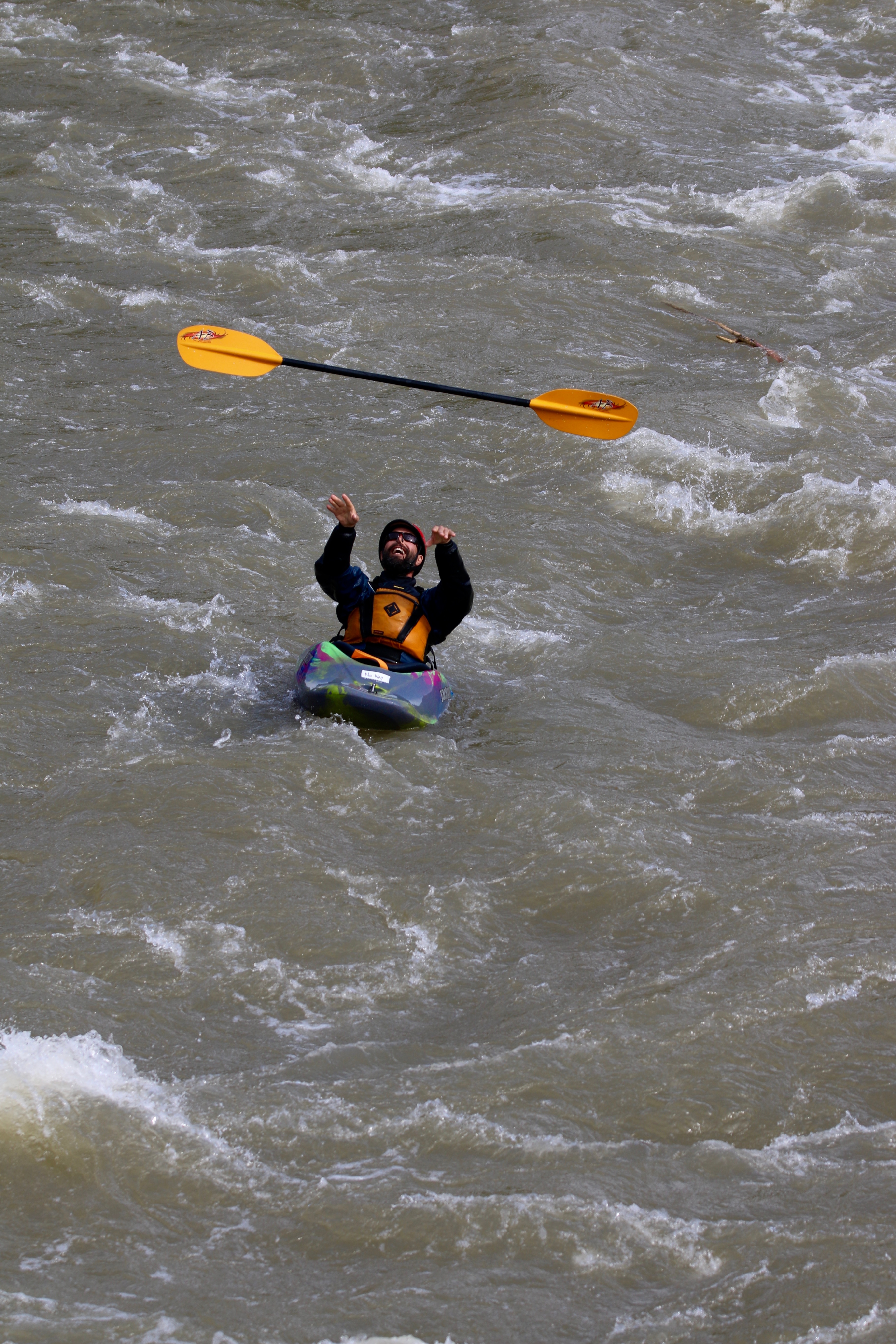 man in a kayak on rough river throwing paddle up in the air
