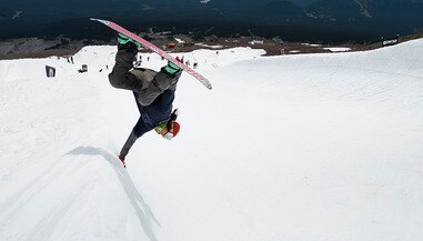 woman doing a snowboard trick flipping on a half pipe course