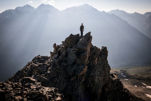 man standing on top of a rocky peak as the sun shines down