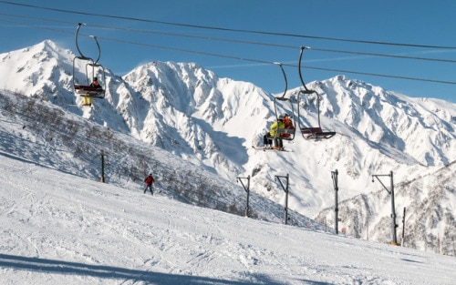 people riding a ski lift on a slope in the mountains