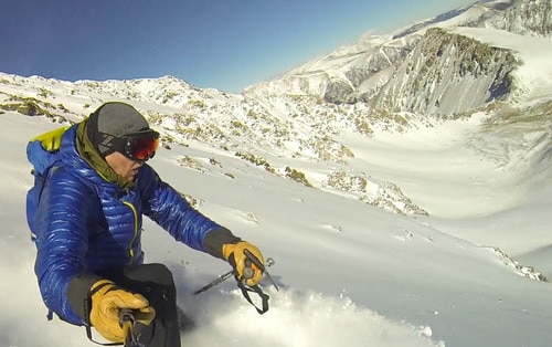 Man holding a selfie stick as he skis down a mountain
