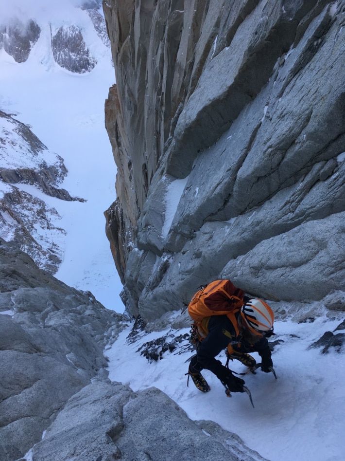 Overhead shot of a man with orange backpack climbing the steep face of a snowy mountain