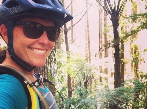 Smiling selfie of a biker with blue helmet and sunglasses biking on a trail