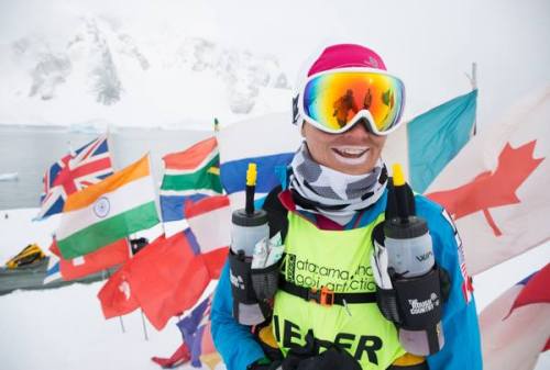 Woman smiling in a racing jersey and snow goggles posing in front of several country’s flags on a snowy mountain
