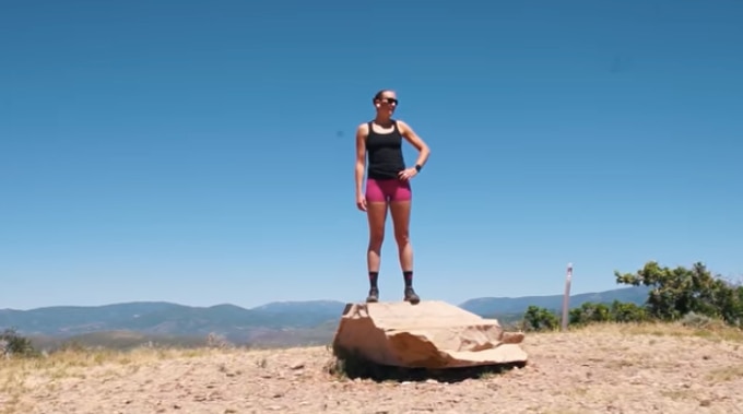 Woman in black tank and pink shorts standing on a rock with a blue sky in the background