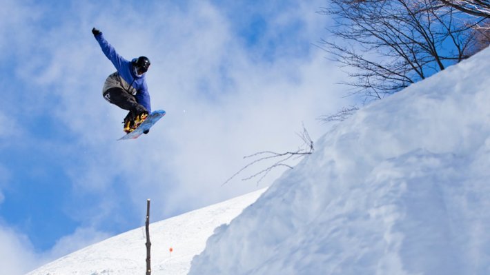 snowboarder in blue coat jumping through the air against blue sky