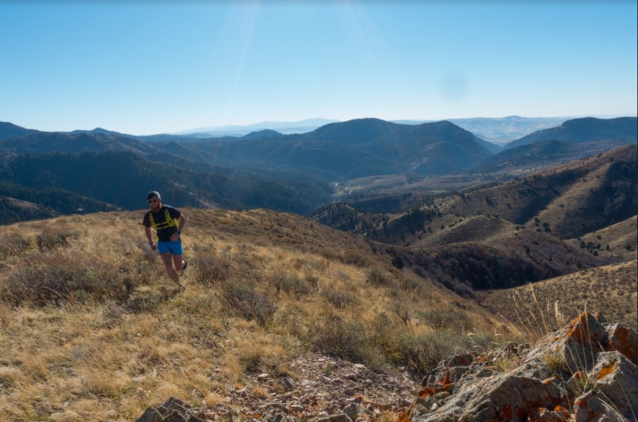 Man running in grassy hills with mountain range in the background