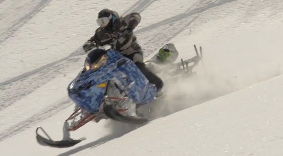 snowboarder riding a blue snowmobile down a snowy hill