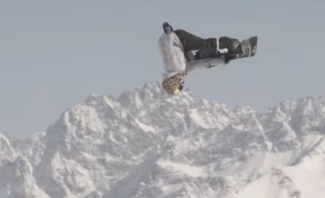 snowboarder flying through the air with snowy mountain in the background