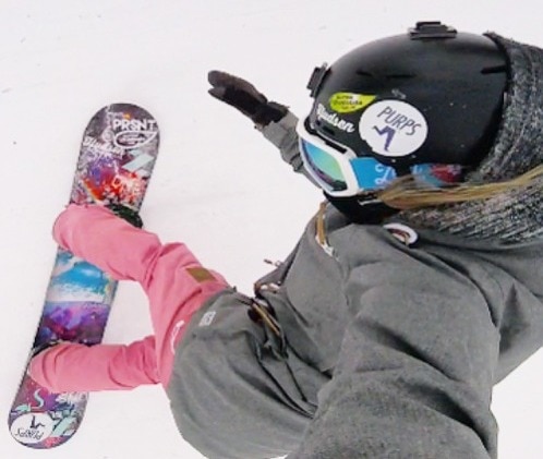 overhead shot of snowboarder wearing pink snow pants and white frame goggles