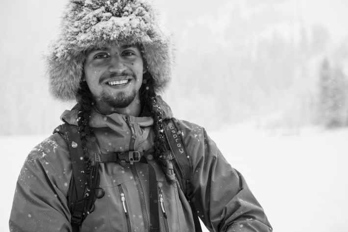 black and white photo of man standing in snow with furry hat and two braids