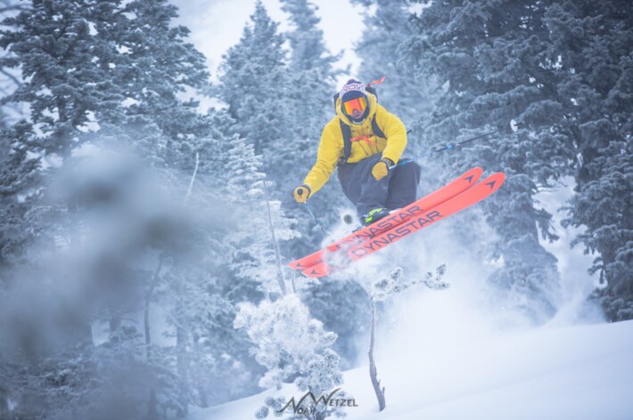 skier in a yellow coat doing a jump in the snow 