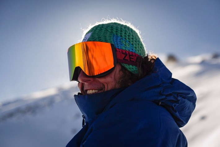man smiling in knit hat and orange lens ski goggles