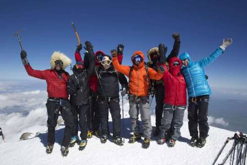 a group of snow hikers cheer at the summit of a mountain