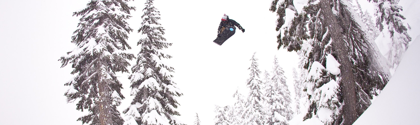 snowboarder getting huge air down mountain with snow covered trees in the background