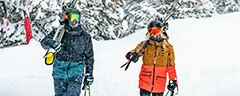 Two snowboarders walking with their gear through the snow